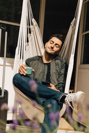 Full length of young man relaxing while sitting in swing against door