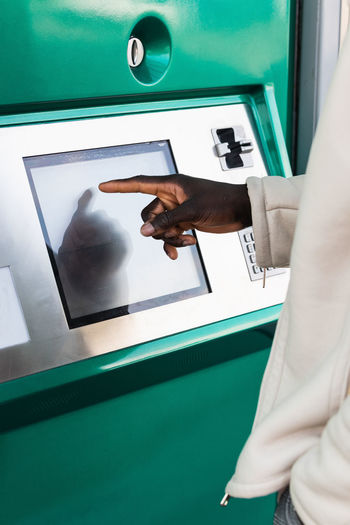 Side view of ethnic cropped unrecognizable male using automated teller machine in city