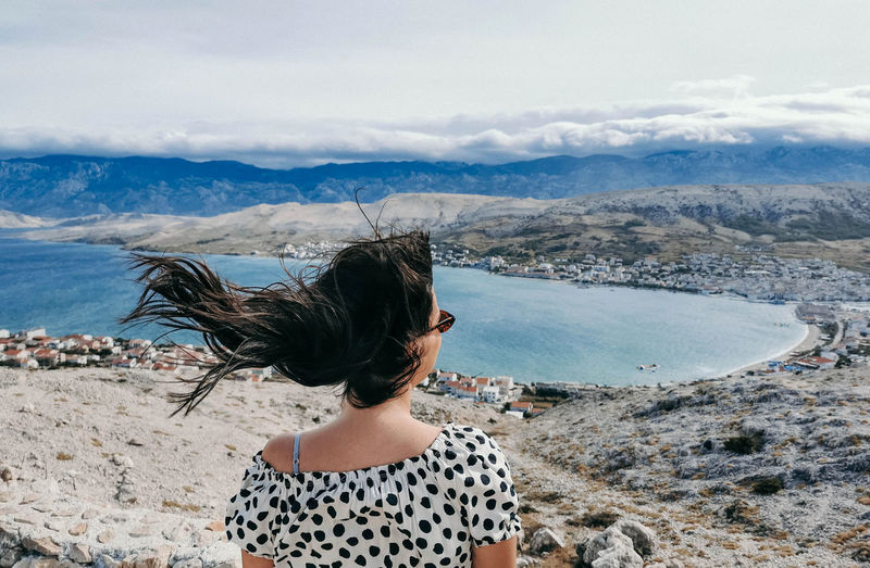 Rear view of young woman on viewpoint over sea. wind blowing hair.
