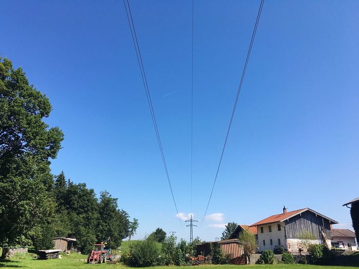 Electricity cable over field against blue sky