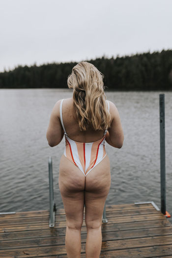 rear view of young woman sitting on pier over lake