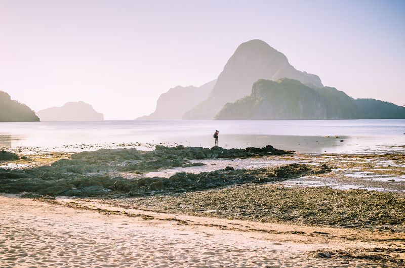 Side view of man standing at beach against clear sky