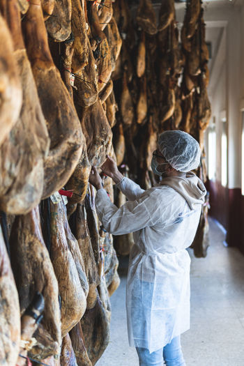 Worker with protective workwear looking at ham in slaughterhouse