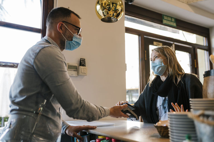 Waiter and female customer discussing while doing contactless payment at a bar