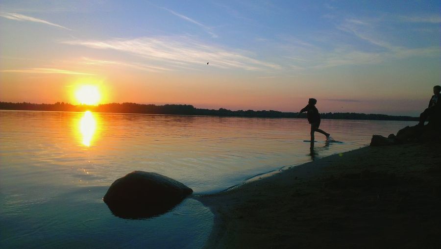 Silhouette boy playing on shore against sky during sunset