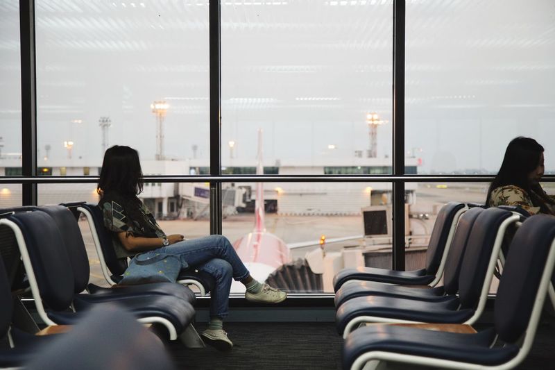 Women sitting on chairs at airport departure area