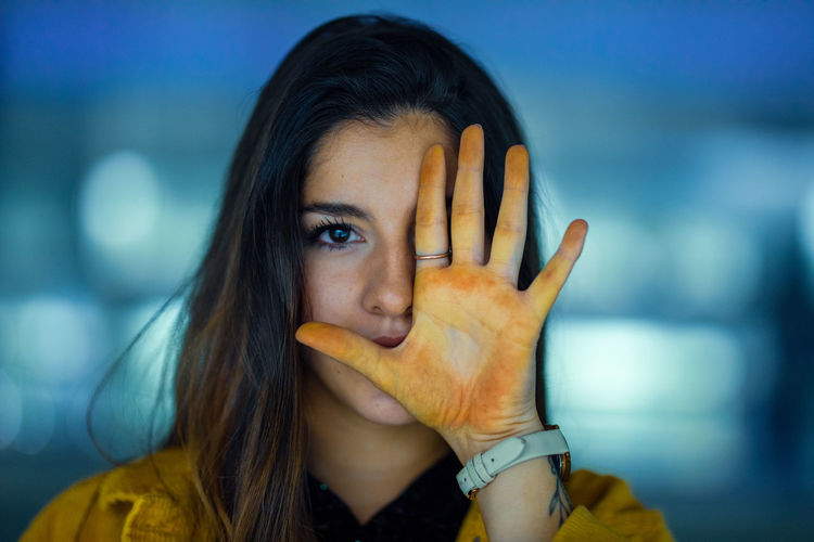 Portrait of young woman with yellow colored palm of hand against face