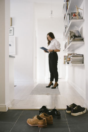 Various shoes on floor with female realtor reading brochure by shelves in background