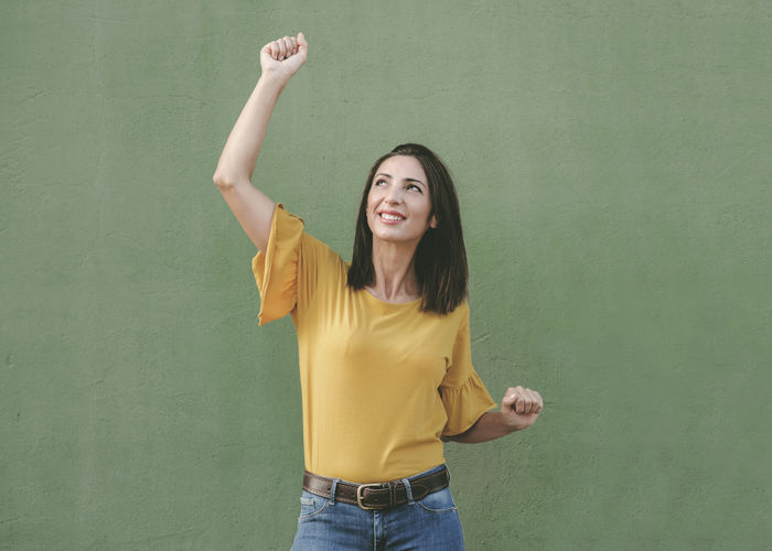 Smiling young woman standing against yellow wall