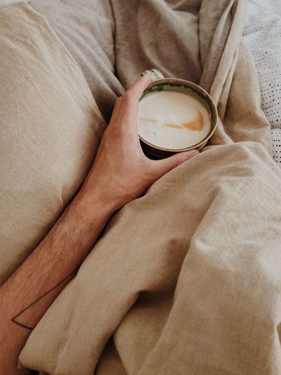 High angle view of hand holding coffee cup on bed
