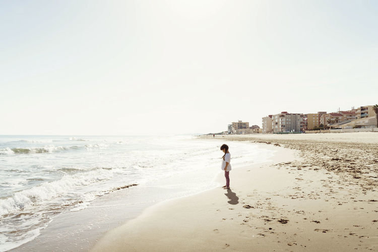 Rear view of woman walking at beach against clear sky