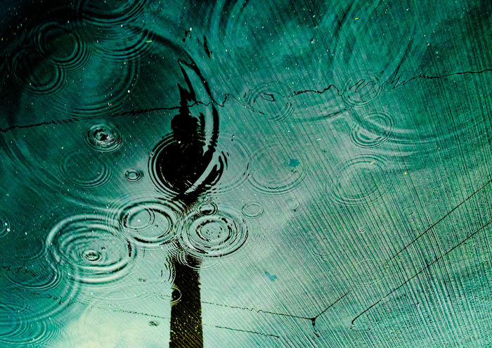 Rain drops falling on a reflection of television tower