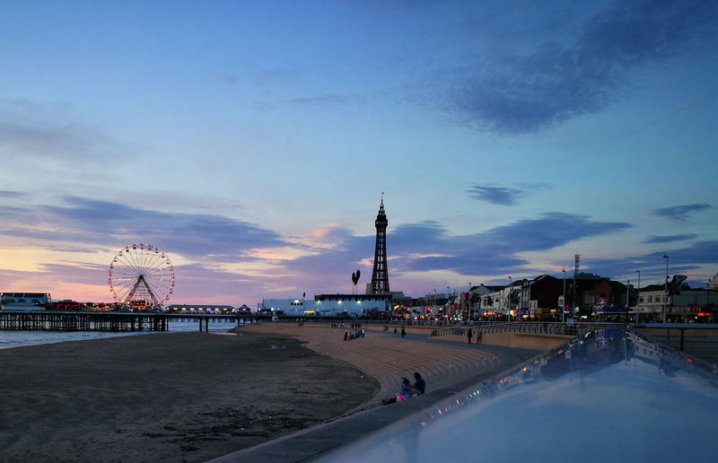 Amusement park by beach against sky during sunset in blackpool