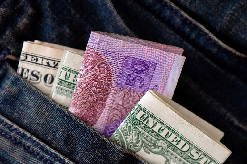 Folded ukrainian hryvnia and american dollars protrude from the pocket of jeans close-up. 