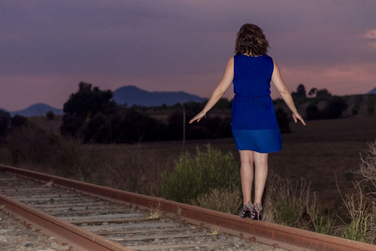 Rear view of woman standing on railroad tracks against sky
