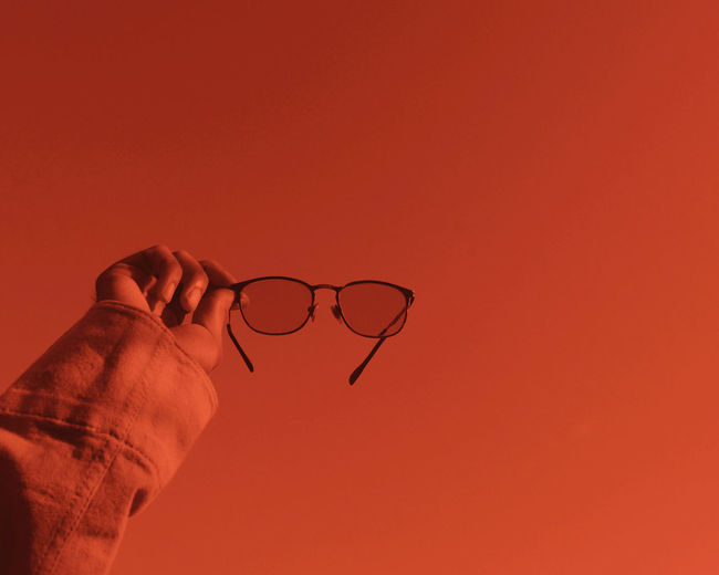 Close-up of hand holding eyeglasses against orange sky