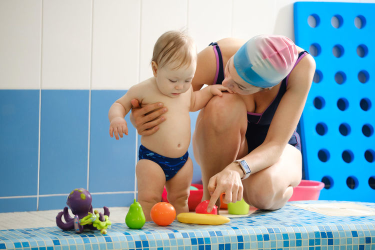 Early age swimming in pool. baby boy waiting near side, learning shapes and fruits. happy child 