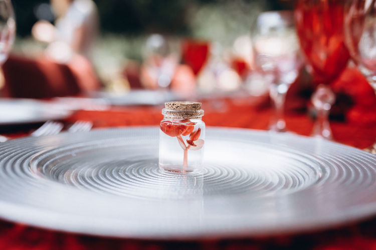 A small red flower in small jar stands on a silver plate against the background of a red tablecloth