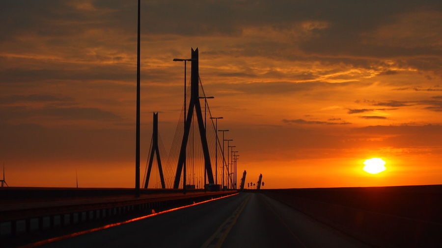 Road by sea against sky during sunset