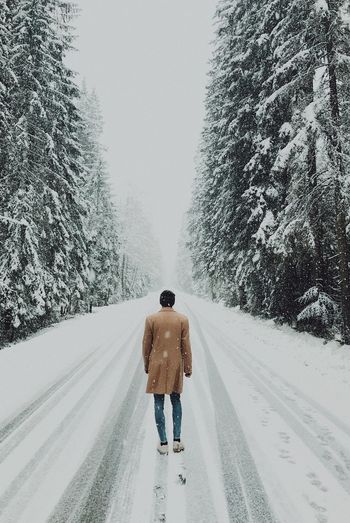 Rear view of man walking on snow covered road