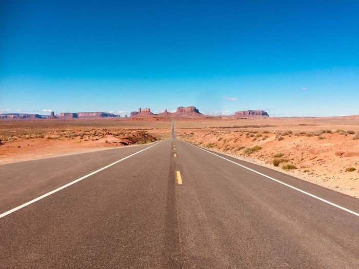 Road passing through desert against blue sky