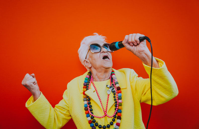 Senior woman singing on microphone against red background