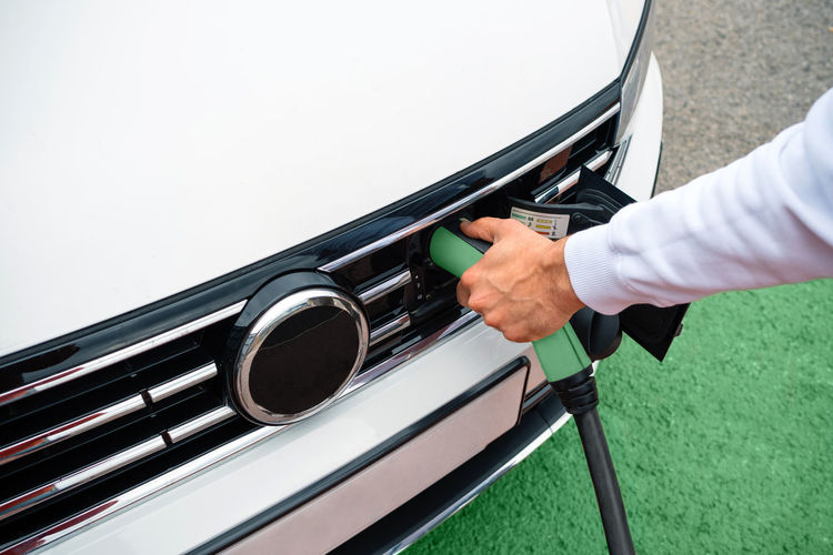 Man hand holding socket plugged into electric car
