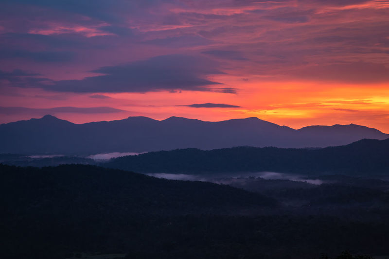 Mountains range misty shadow with dramatic colorful sunset sky at dusk from flat angle
