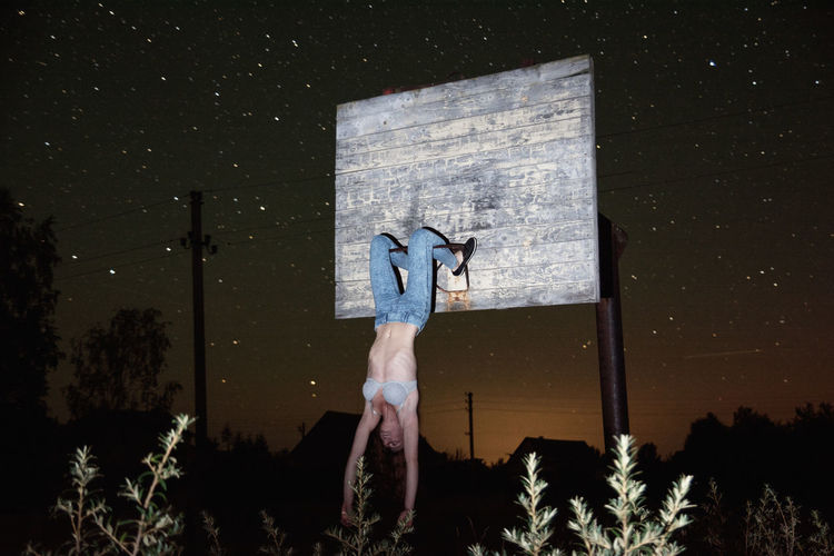Young woman hanging on abandoned basketball hoop at night