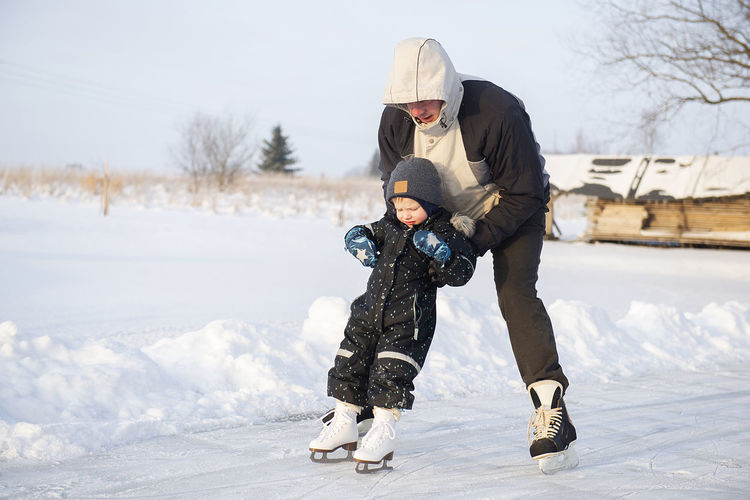 Grandfather teaching her little grandson ice skating at outdoor skating rink.