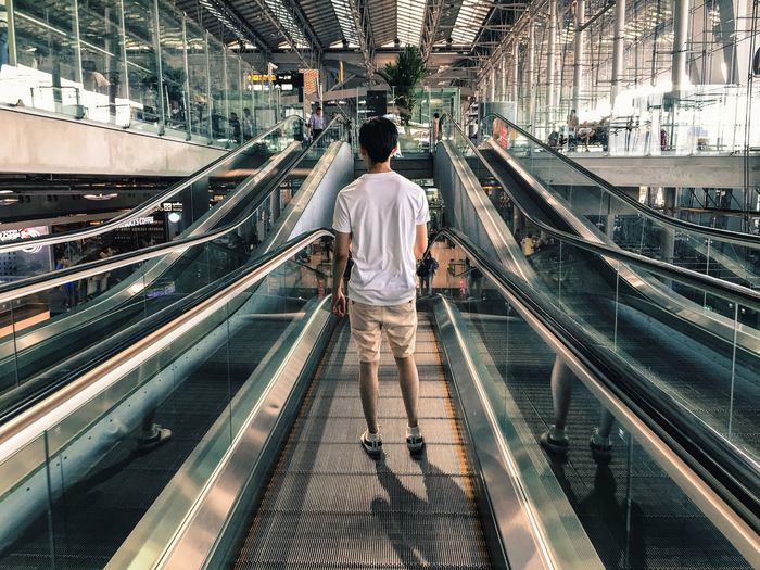 Rear view of man standing on escalator at airport