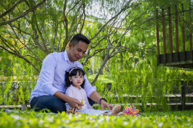 Full length of father and daughter sitting on grass outdoors