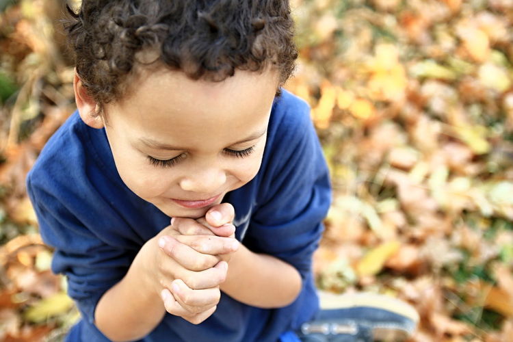 High angle view of cute boy with eyes closed and hands clasped praying in park during autumn