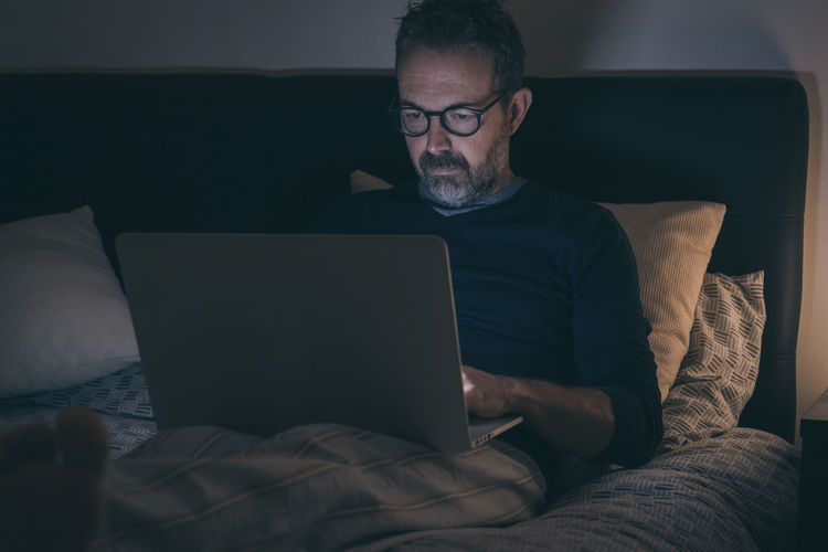 Man works with laptop lying on bed. male home working with remote office. boy sitting in bedroom 