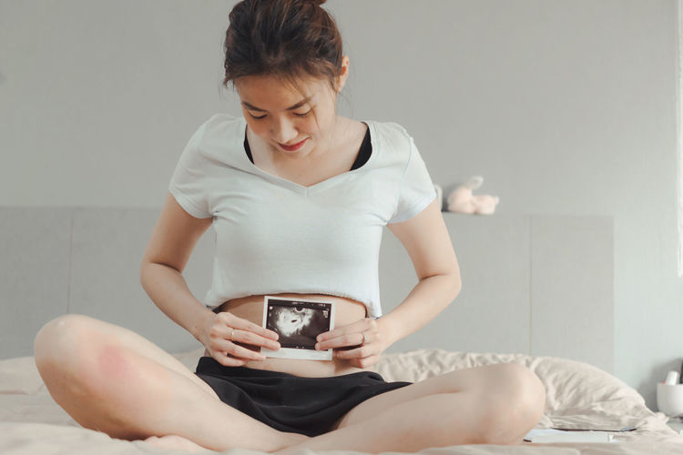 Young woman using mobile phone while sitting on bed