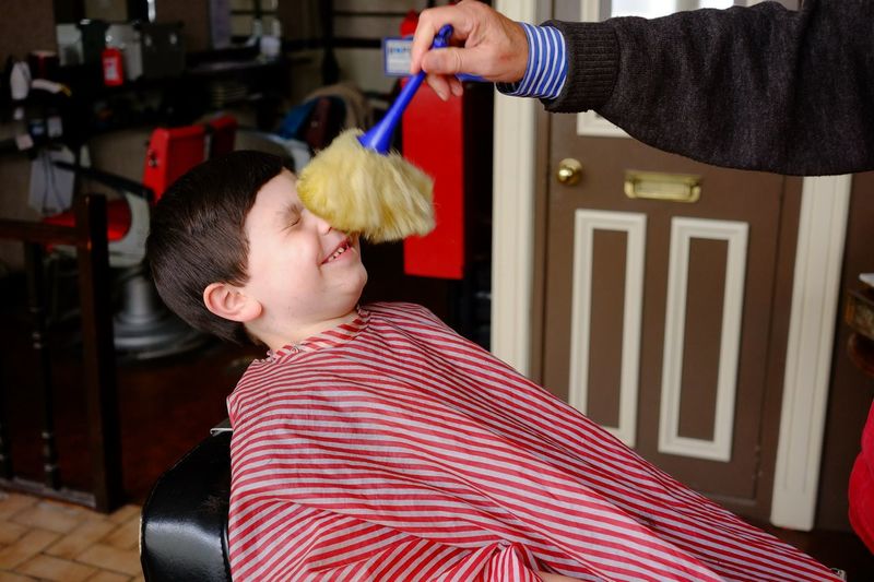 Barber brushing hair from boy face in barber shop