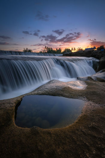 Scenic view of waterfall against sky during sunset