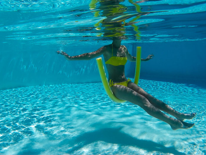 Underwater view of woman sitting on swimming noodle