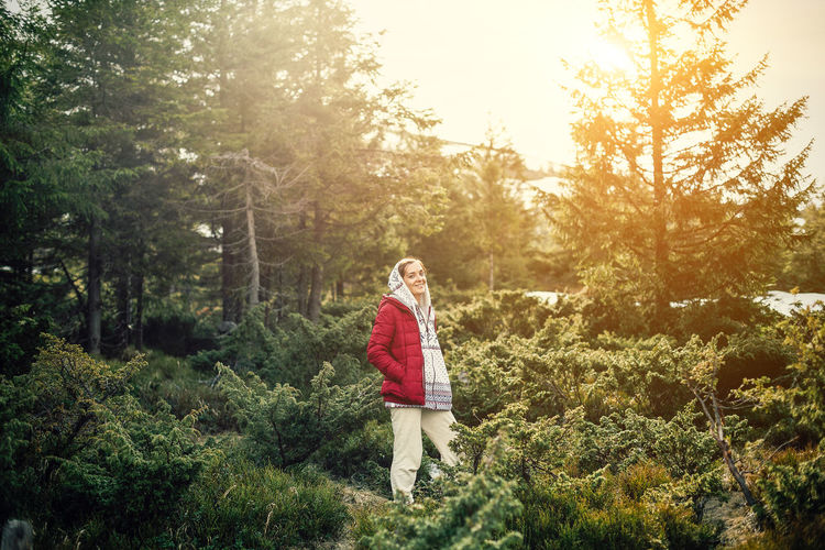 Portrait of smiling woman wearing warm clothing standing amidst plants in forest