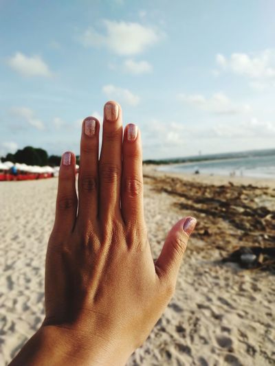 Close-up of hand on sea shore against sky