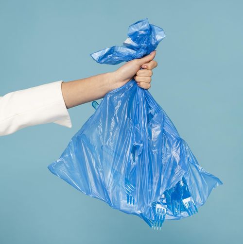 Cropped hand of woman holding plastic bag against white background