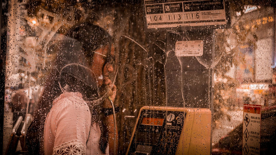 Teenage girl talking in wet telephone booth during rain