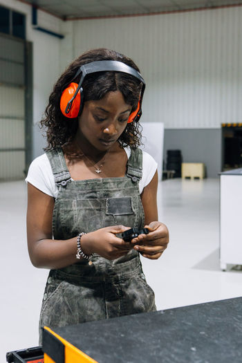Professional young african american female mechanic in apron and protective headphones taking tools from box while working in modern repair service workshop