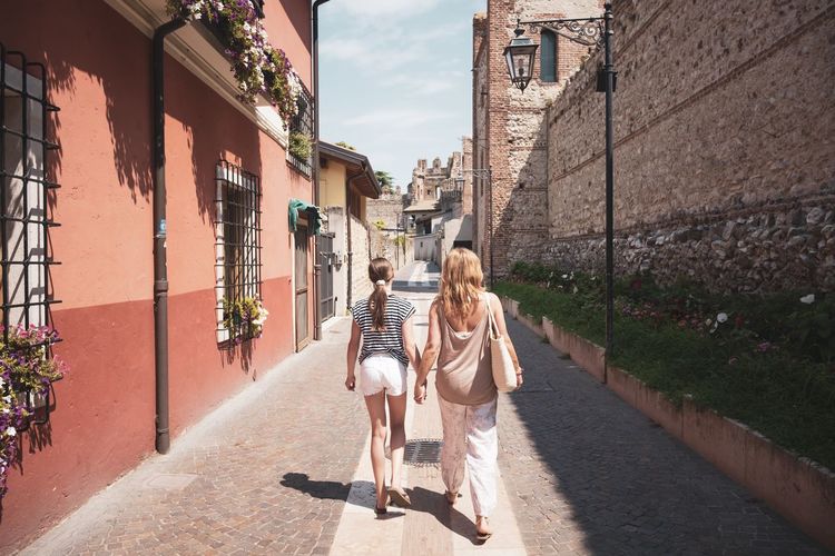 Rear view of mother and daughter walking ahead through the streets of a small village in italy
