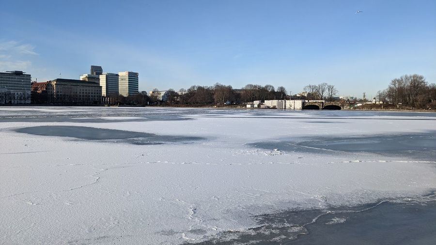 Frozen lake by buildings against clear sky