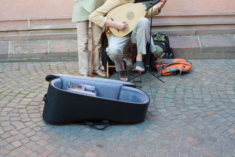 Low section of man with friend playing musical instrument on street