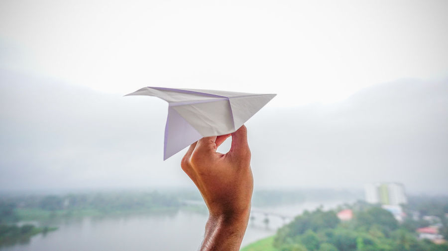 Close-up of hand holding paper plane against sky