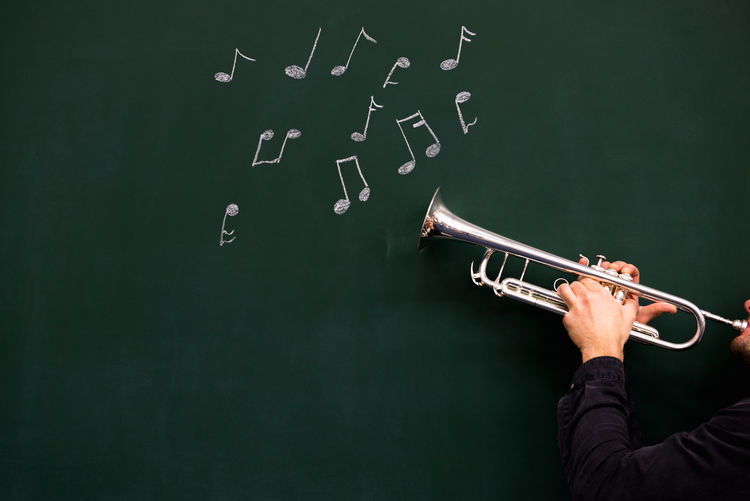 Cropped hands of man holding trumpet by musical notes on blackboard