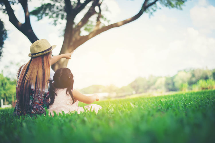 Rear view of mother and daughter sitting on grassy field in park