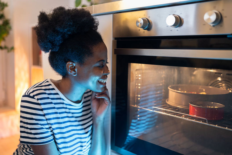 Impatient black girl sitting next to oven door while making homemade cake for husband birthday